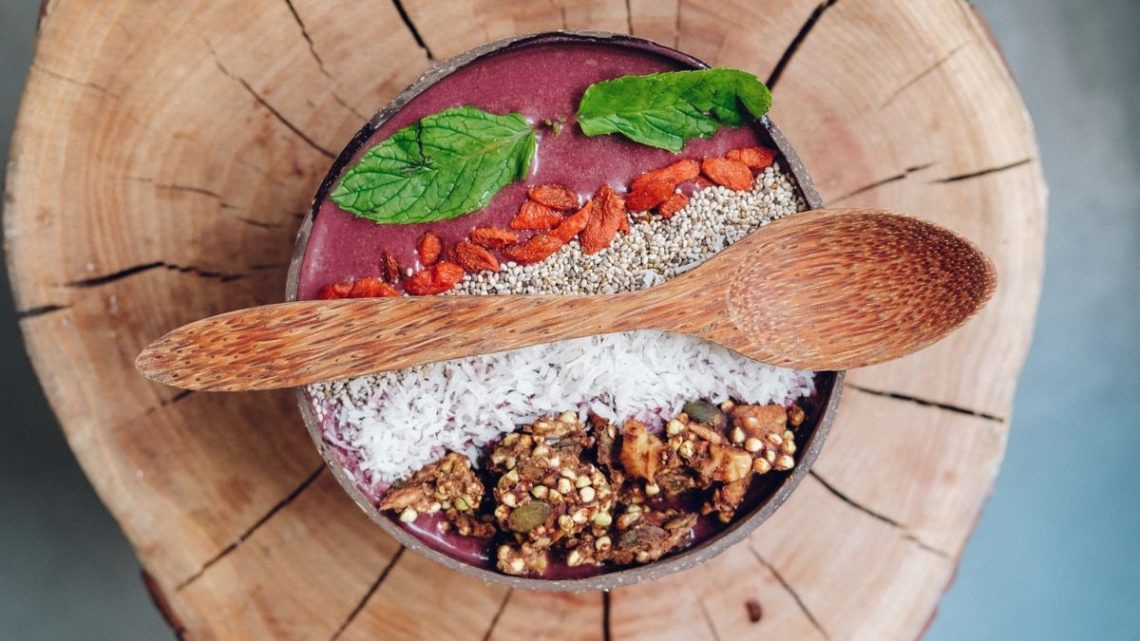 Healthy acai bowl with granola, mint leaves, and berries served on rustic wood.
