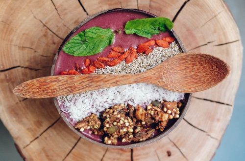 Healthy acai bowl with granola, mint leaves, and berries served on rustic wood.